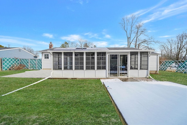 back of property with solar panels, a sunroom, a yard, and a patio area