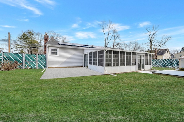 back of property featuring a sunroom, a yard, a patio area, and solar panels