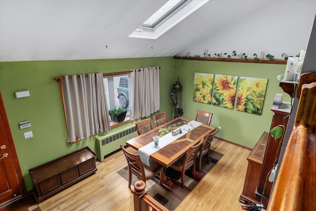 dining space with lofted ceiling with skylight, radiator, and light hardwood / wood-style flooring