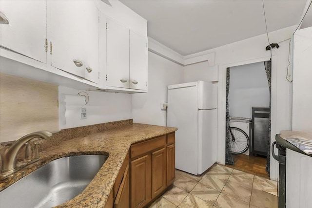 kitchen with white cabinetry, sink, light stone counters, and white refrigerator