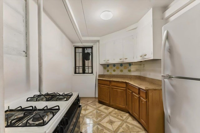 kitchen featuring white refrigerator, white cabinetry, and gas range oven