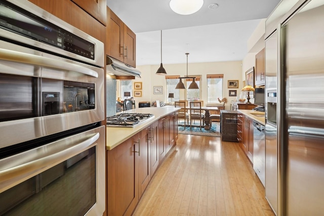 kitchen featuring tasteful backsplash, stainless steel appliances, hanging light fixtures, and light wood-type flooring