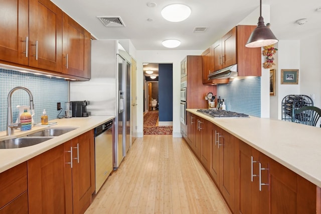 kitchen with sink, hanging light fixtures, stainless steel appliances, light hardwood / wood-style floors, and decorative backsplash