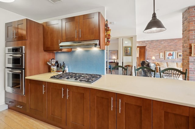 kitchen featuring appliances with stainless steel finishes, pendant lighting, brick wall, light hardwood / wood-style floors, and decorative backsplash