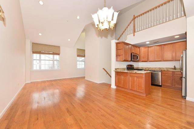 kitchen featuring appliances with stainless steel finishes, pendant lighting, high vaulted ceiling, light hardwood / wood-style floors, and an inviting chandelier