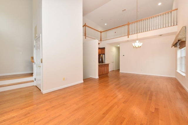 unfurnished living room featuring an inviting chandelier, a high ceiling, and light wood-type flooring