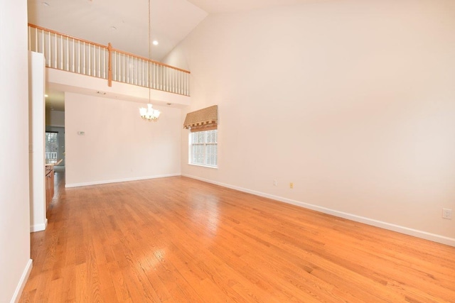 empty room with high vaulted ceiling, light wood-type flooring, and a chandelier