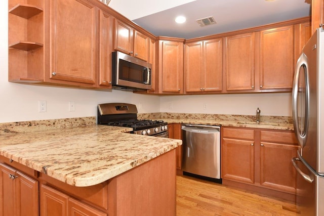 kitchen with sink, kitchen peninsula, stainless steel appliances, light stone countertops, and light wood-type flooring