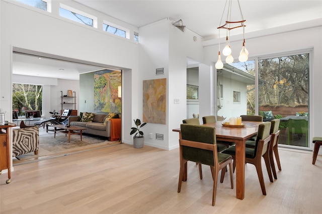 dining space with visible vents, light wood-style flooring, a high ceiling, and baseboards