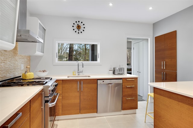 kitchen featuring brown cabinets, a sink, stainless steel appliances, wall chimney exhaust hood, and tasteful backsplash