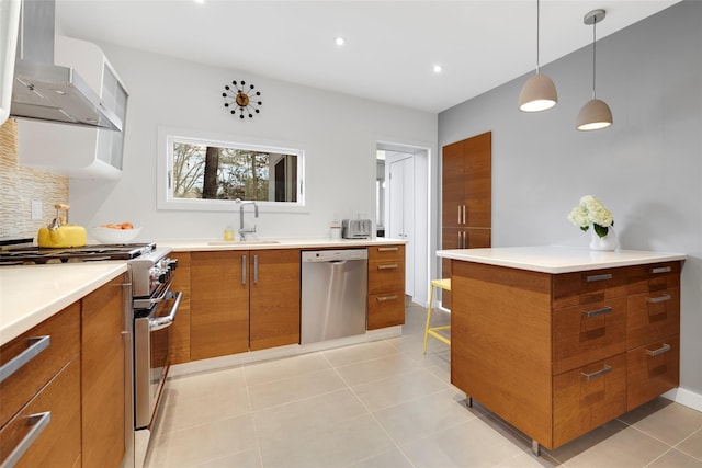 kitchen with brown cabinetry, a sink, decorative backsplash, appliances with stainless steel finishes, and wall chimney exhaust hood