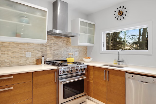 kitchen with backsplash, wall chimney range hood, brown cabinets, appliances with stainless steel finishes, and a sink