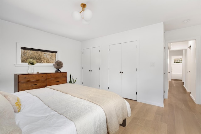 bedroom with baseboards, multiple closets, and light wood-style flooring