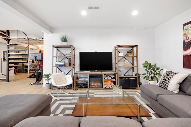 living area featuring a glass covered fireplace, recessed lighting, wood finished floors, and visible vents