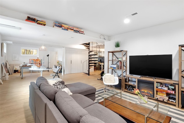 living area with visible vents, a warm lit fireplace, and wood finished floors