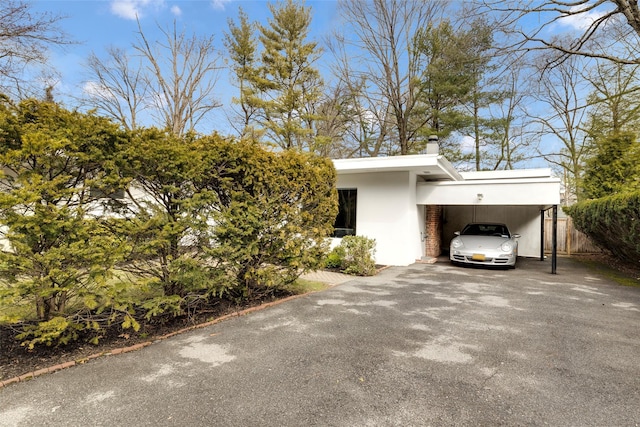 view of side of home featuring stucco siding, aphalt driveway, fence, an attached carport, and a chimney