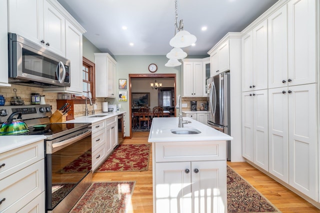 kitchen featuring sink, white cabinetry, decorative light fixtures, appliances with stainless steel finishes, and a kitchen island with sink