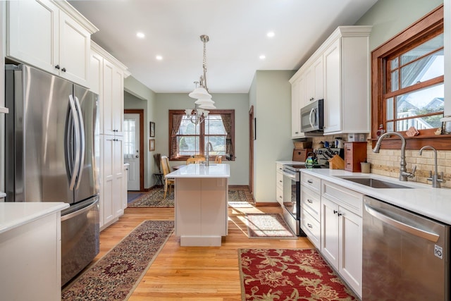 kitchen featuring sink, a center island, hanging light fixtures, stainless steel appliances, and white cabinets