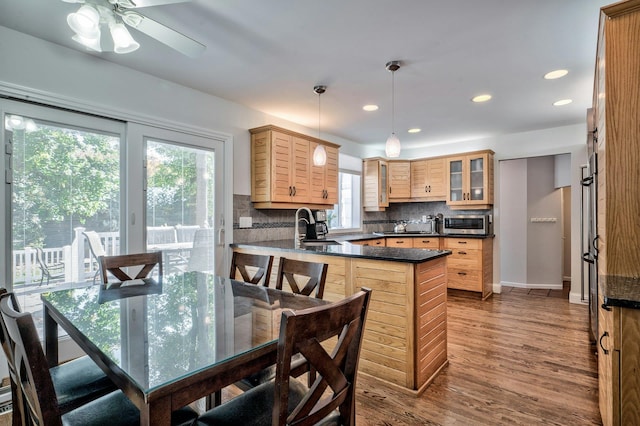 kitchen featuring tasteful backsplash, wood-type flooring, decorative light fixtures, kitchen peninsula, and light brown cabinets