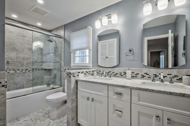 full bathroom featuring toilet, vanity, shower / bath combination with glass door, and tile walls