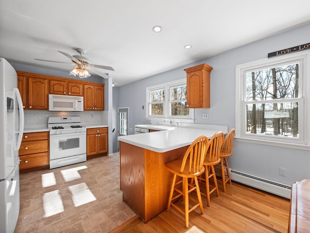 kitchen with kitchen peninsula, a baseboard heating unit, white appliances, a breakfast bar area, and decorative backsplash