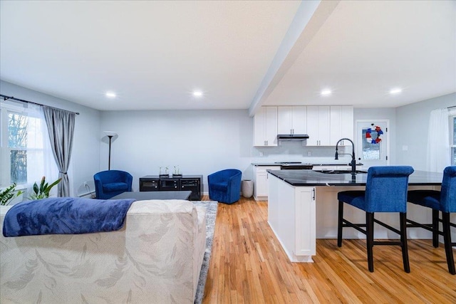 kitchen featuring sink, light hardwood / wood-style flooring, a breakfast bar, an island with sink, and white cabinets