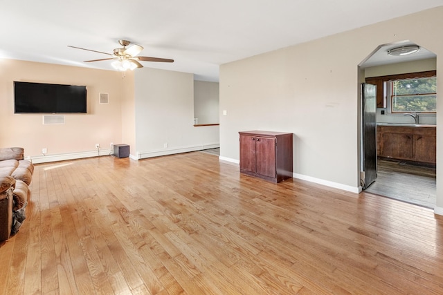 unfurnished living room with a baseboard heating unit, light hardwood / wood-style floors, sink, and ceiling fan