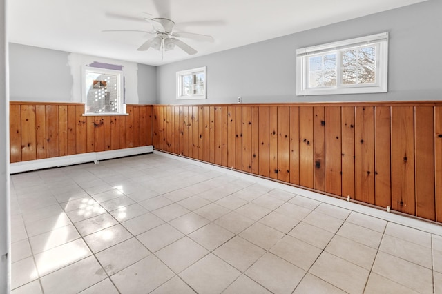 spare room with baseboard heating, ceiling fan, plenty of natural light, and wood walls