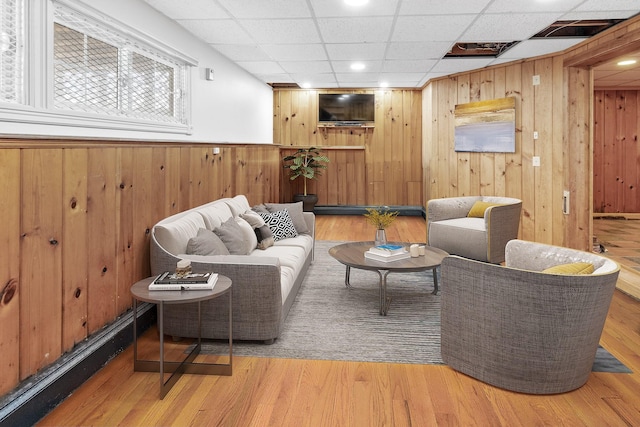 living room with a baseboard radiator, wooden walls, a drop ceiling, and light wood-type flooring