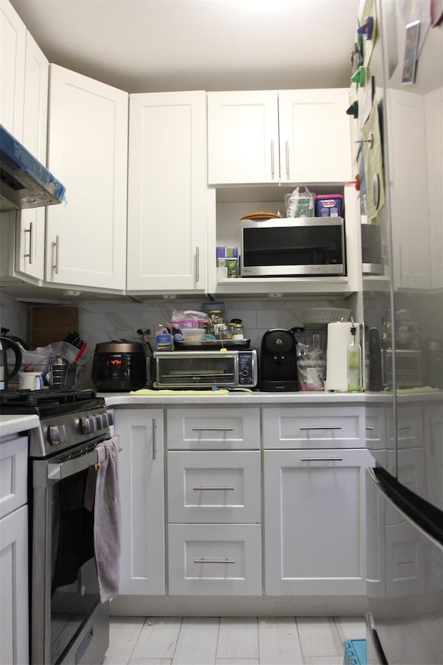 kitchen featuring tasteful backsplash, stainless steel appliances, exhaust hood, and white cabinets