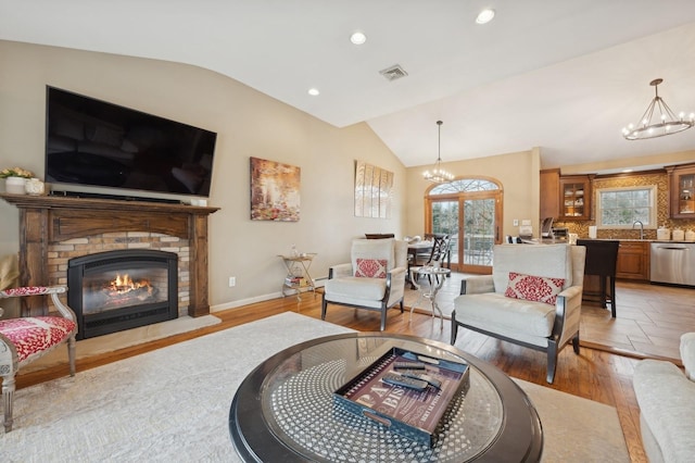 living room featuring an inviting chandelier, lofted ceiling, sink, and light hardwood / wood-style floors