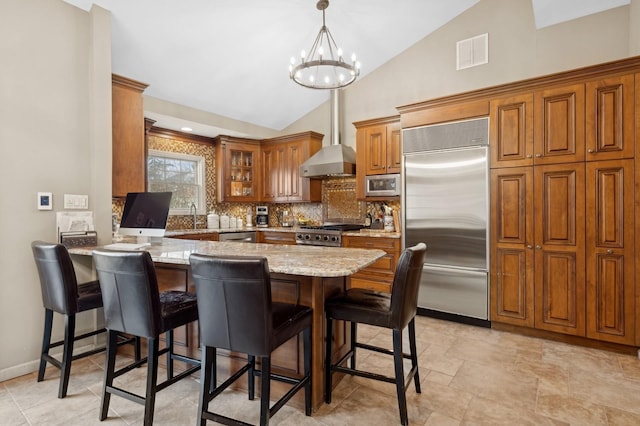 kitchen with built in appliances, hanging light fixtures, kitchen peninsula, a notable chandelier, and light stone countertops