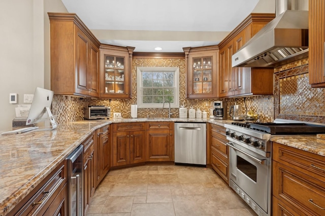 kitchen with light stone countertops, appliances with stainless steel finishes, sink, and wall chimney range hood