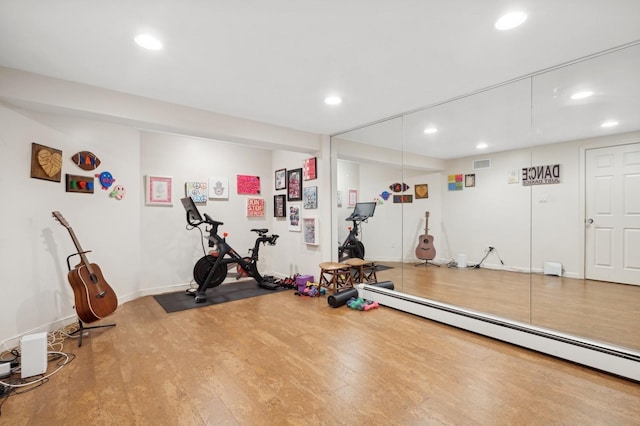 exercise area with hardwood / wood-style flooring and a baseboard heating unit