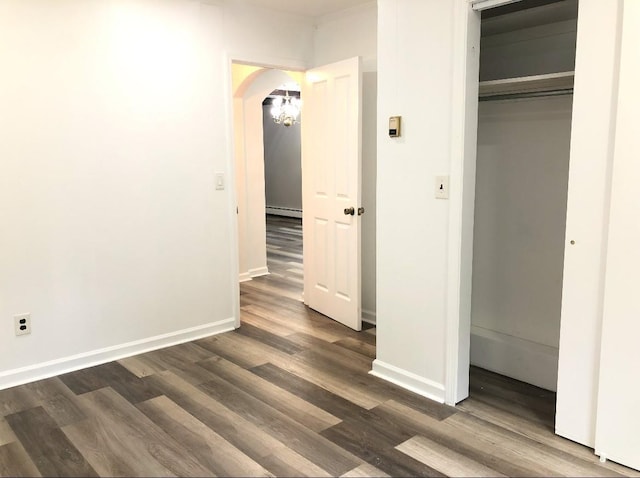 unfurnished bedroom with a baseboard heating unit, dark hardwood / wood-style floors, and a closet