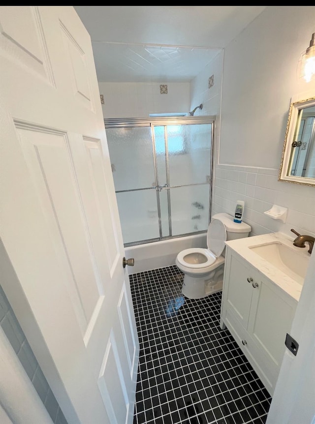 full bathroom with tile walls, tile patterned flooring, bath / shower combo with glass door, vanity, and toilet