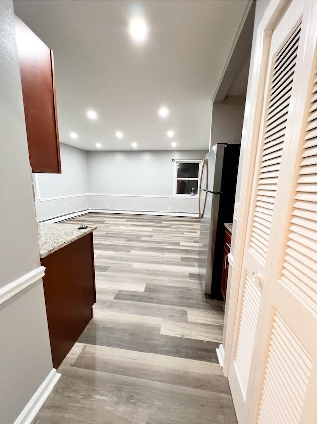 kitchen with stainless steel refrigerator, light hardwood / wood-style floors, and light stone counters