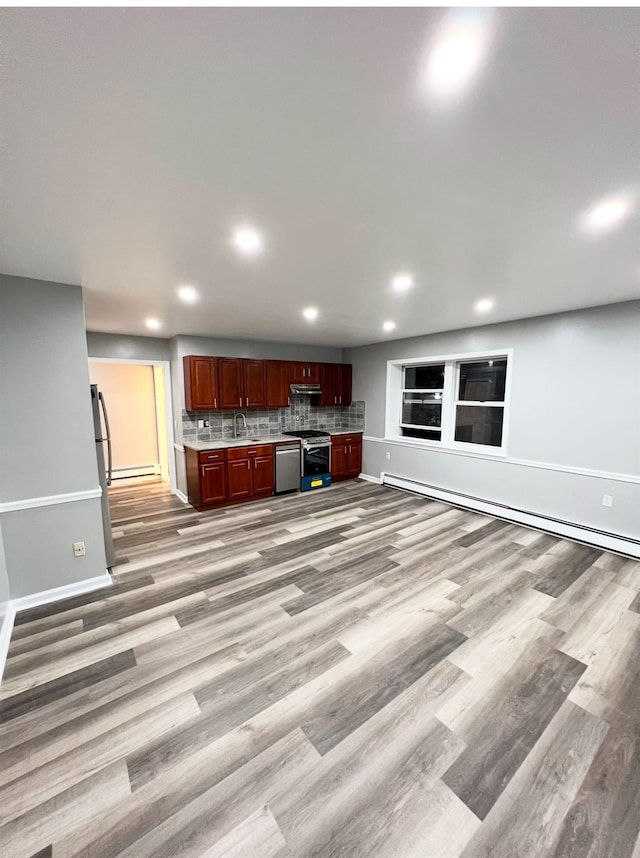 kitchen with sink, backsplash, stainless steel appliances, light hardwood / wood-style floors, and a baseboard heating unit