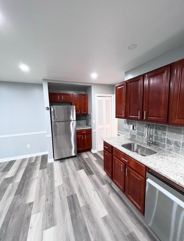 kitchen featuring sink, light hardwood / wood-style flooring, stainless steel appliances, light stone countertops, and decorative backsplash