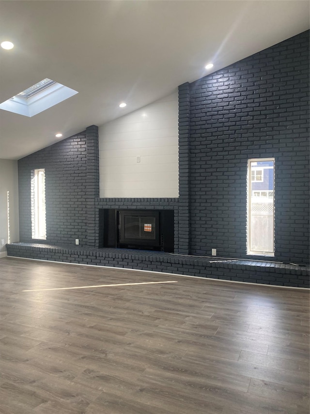 unfurnished living room featuring hardwood / wood-style flooring, vaulted ceiling, and brick wall