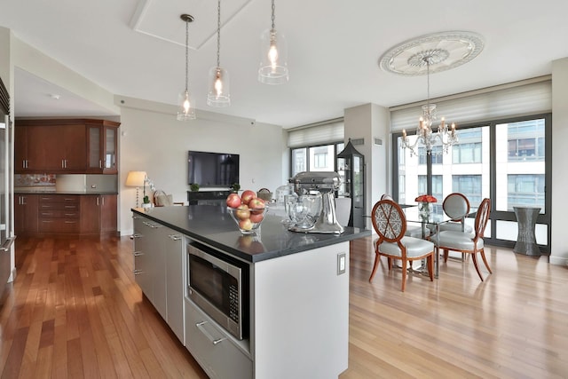 kitchen featuring pendant lighting, a center island, stainless steel microwave, and light wood-type flooring