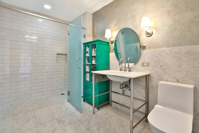 bathroom with toilet, a shower with shower door, sink, and tile walls