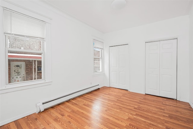 unfurnished bedroom with light wood-type flooring, multiple closets, and baseboard heating