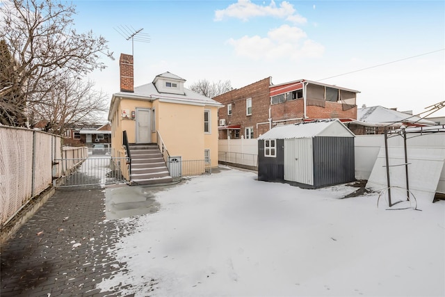 snow covered rear of property with a storage unit