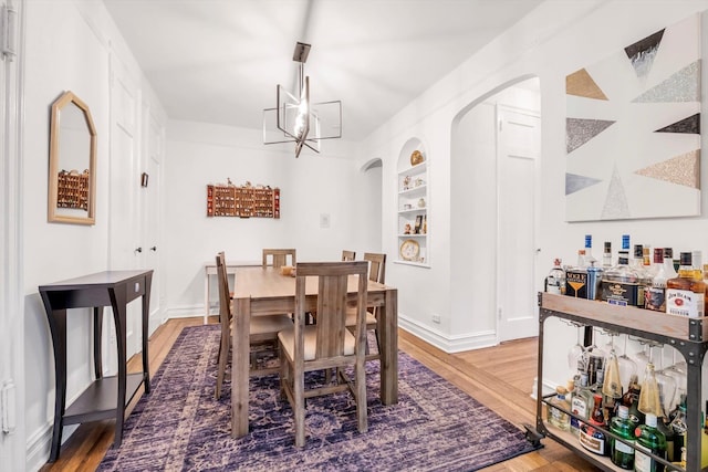 dining space featuring a chandelier, built in shelves, and wood finished floors