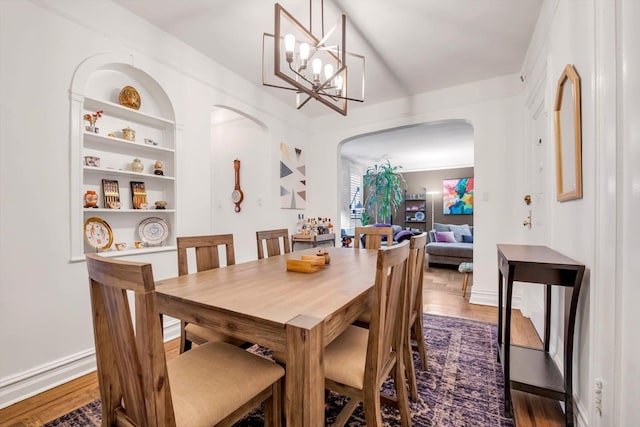 dining space featuring an inviting chandelier, built in shelves, arched walkways, and dark wood finished floors