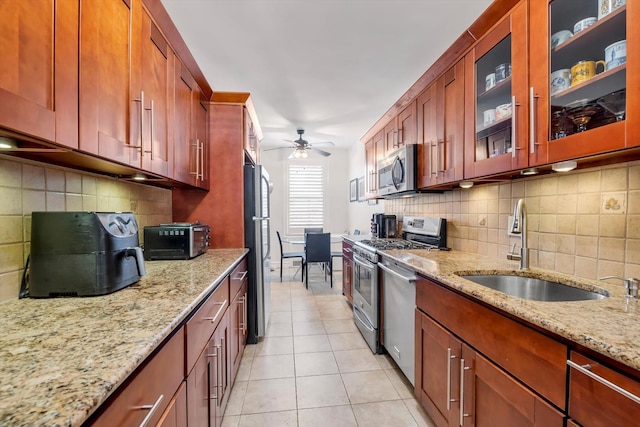 kitchen with light tile patterned floors, ceiling fan, appliances with stainless steel finishes, light stone counters, and a sink