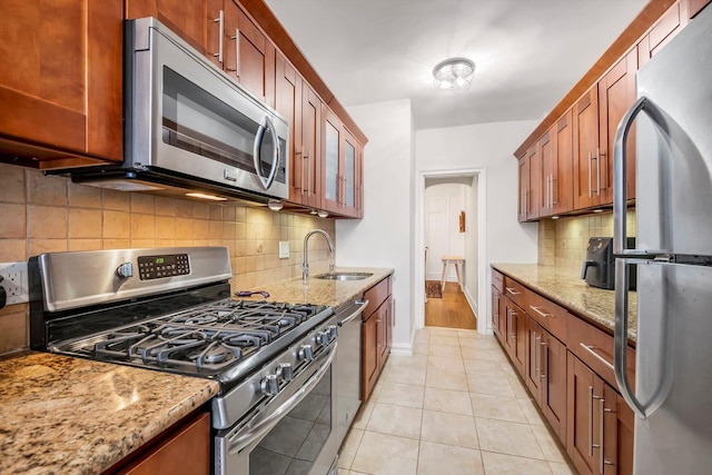 kitchen with light tile patterned floors, light stone counters, a sink, appliances with stainless steel finishes, and glass insert cabinets