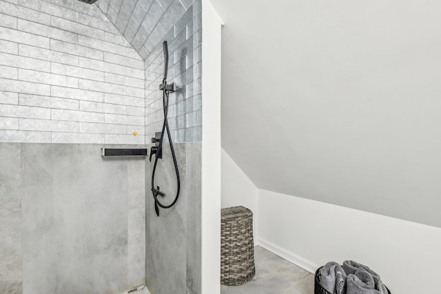 bathroom with vaulted ceiling, a tile shower, and concrete floors