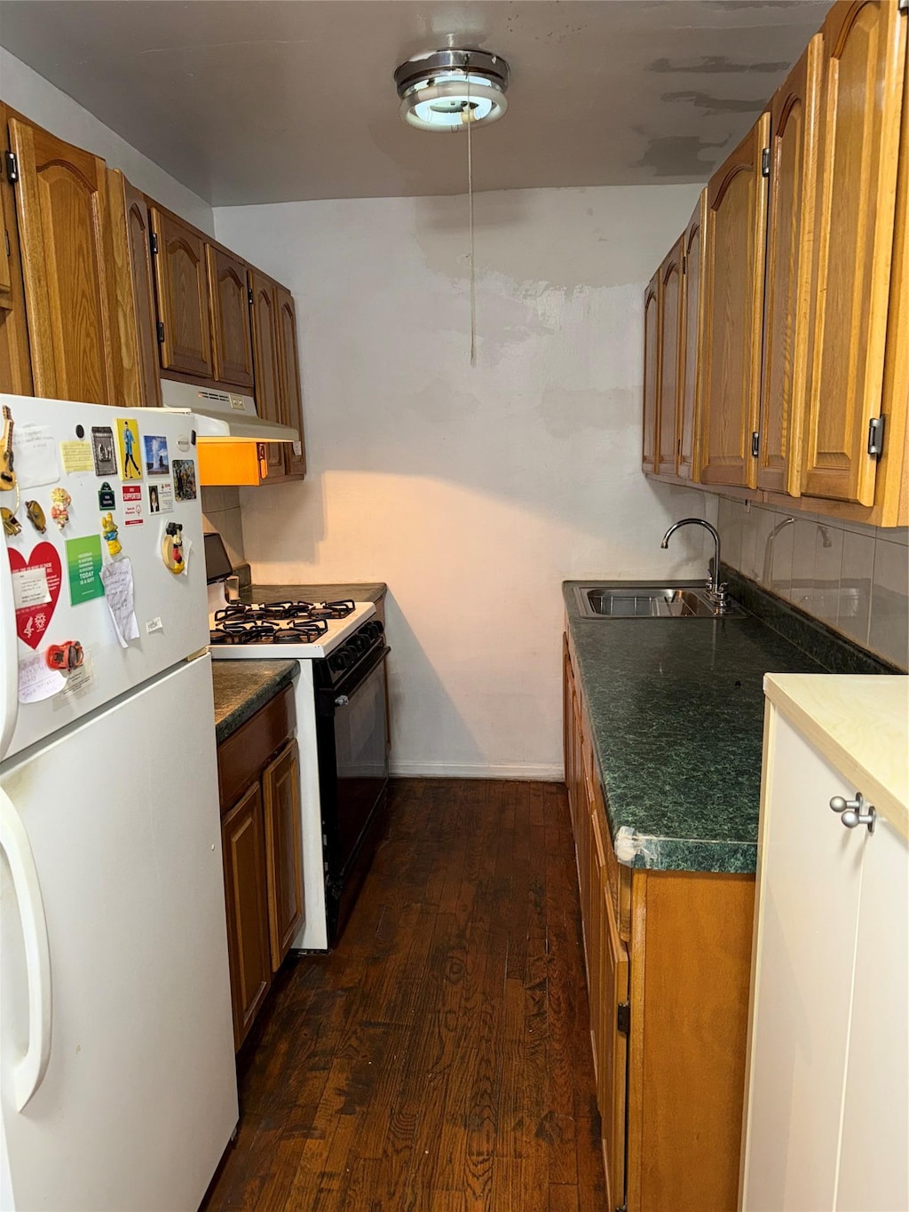 kitchen featuring sink, tasteful backsplash, white refrigerator, dark hardwood / wood-style floors, and black gas range